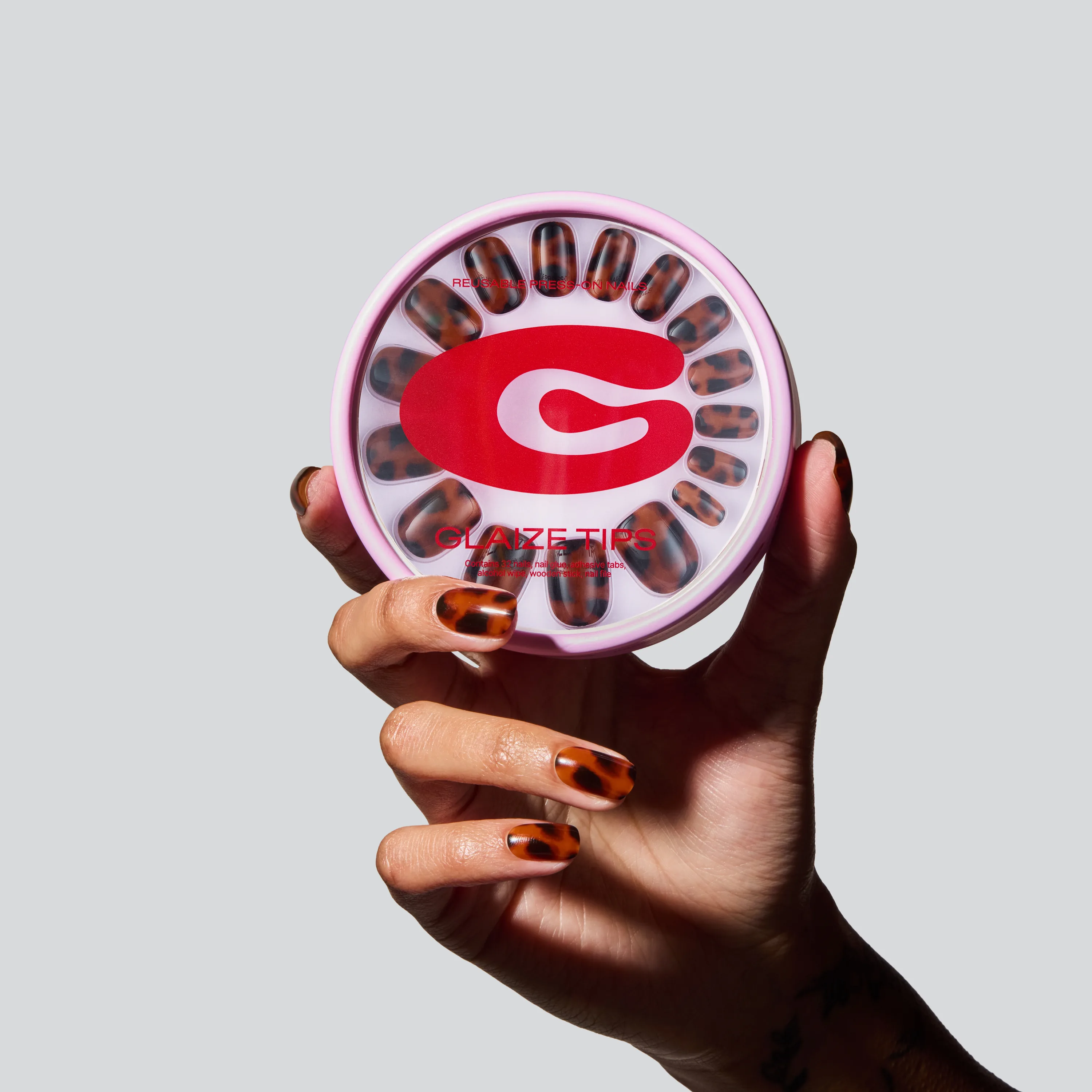 A hand holding a pack of Tortoise Shell Glaize Tips press-on nails